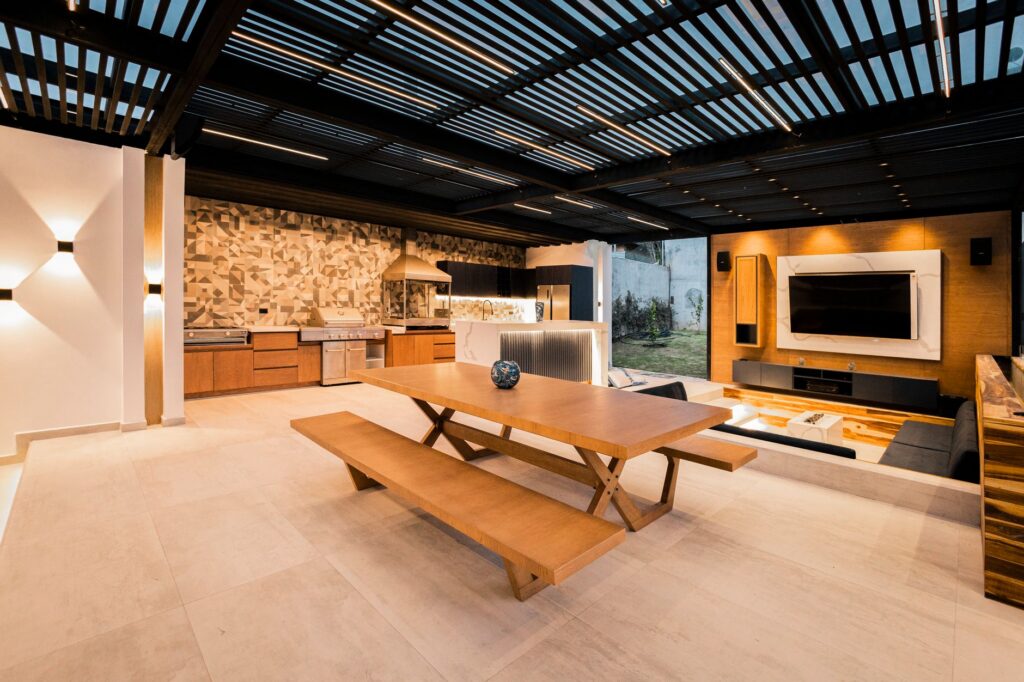 Covered outdoor kitchen with a slatted roof, built-in grill and dining table