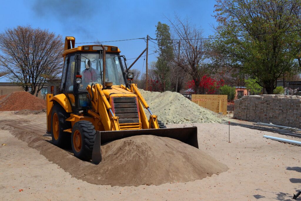 Excavator moving soil and sand during site preparation for a patio base
