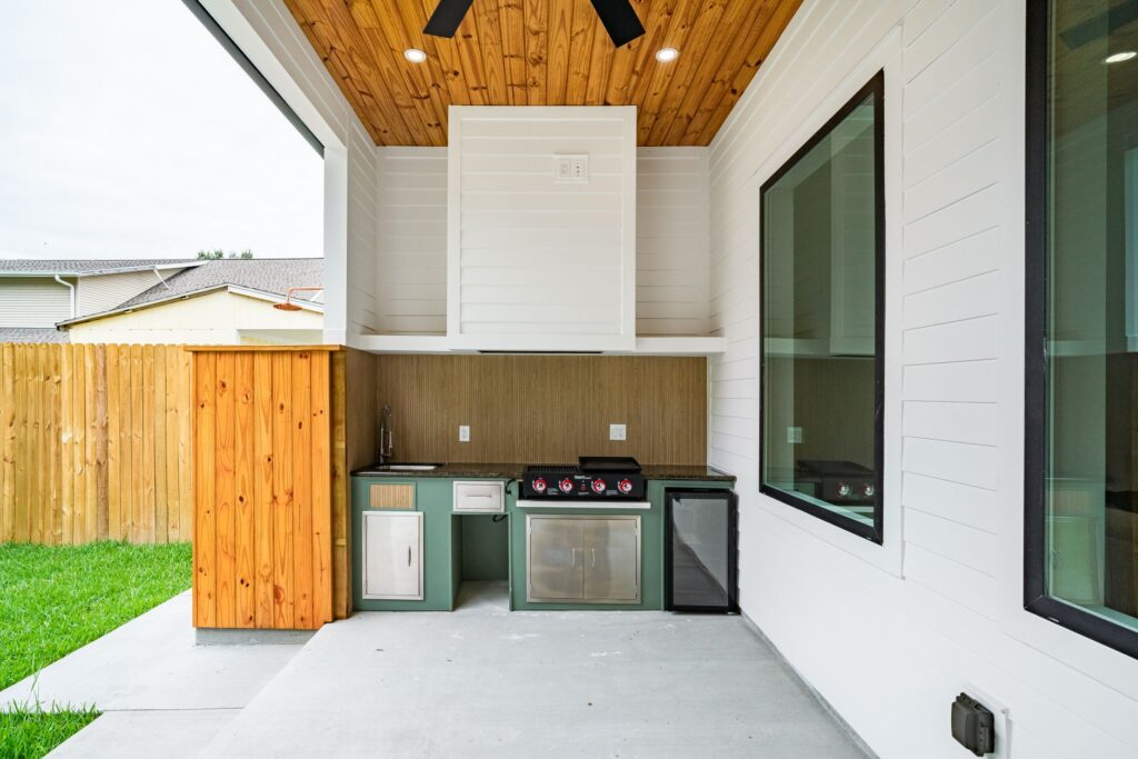 Covered outdoor kitchen with a built-in grill and cabinetry in a backyard