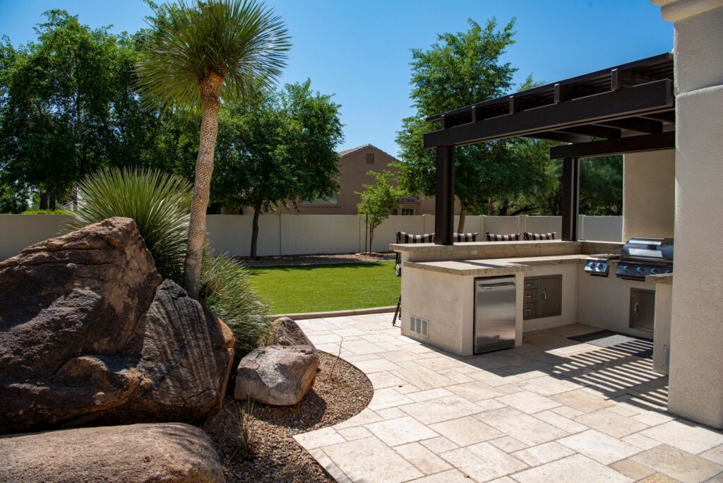 Built-in outdoor kitchen with grill and stone counter on a landscaped patio