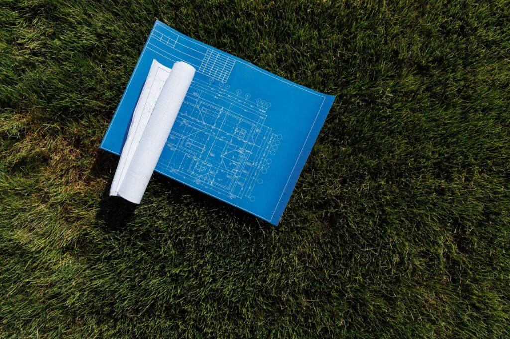 Rolled patio design plans and blueprints laid out on a grass lawn