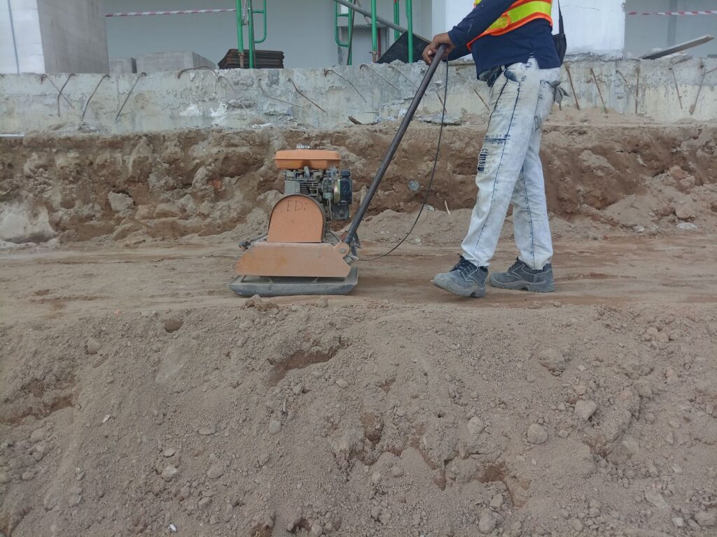 Worker compacting the soil base with a plate compactor before paving begins